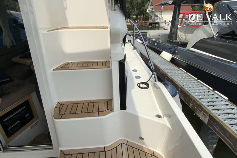 Een witte boot met teakhouten treden en een reling, afgemeerd aan een steiger met een andere boot ernaast. — Galeon 300 Fly