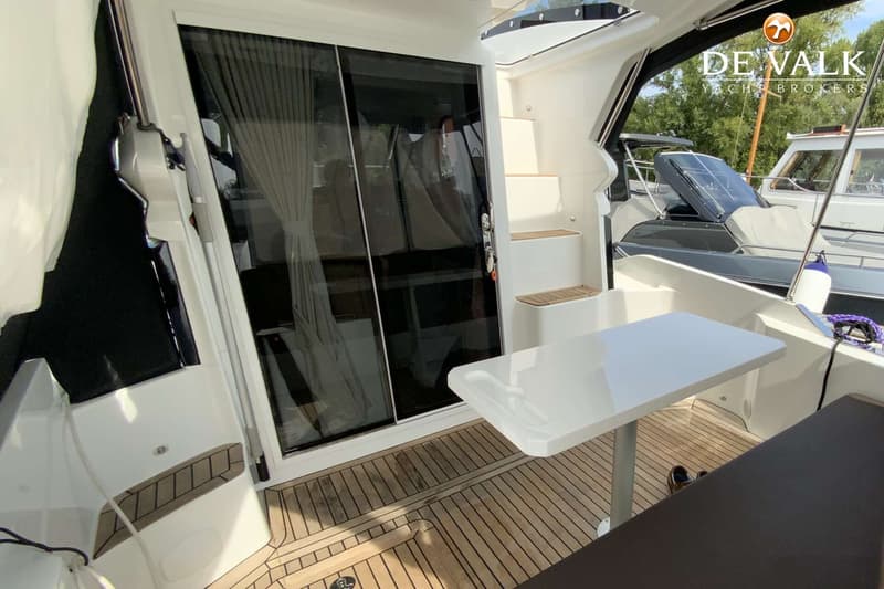 Een bootinterieur met een glazen schuifdeur, een witte tafel, een houten vloer en een trapje.