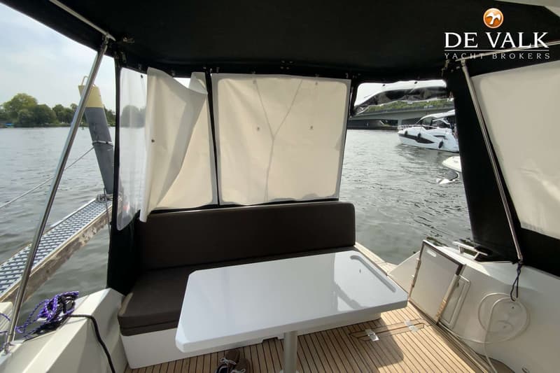 Een bootinterieur met een tafel, bank en uitzicht op water met een andere boot en een brug. — Galeon 300 Fly