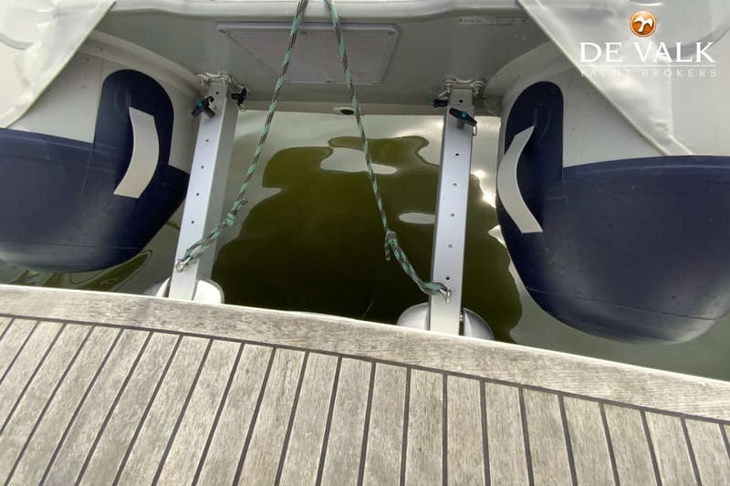 Een houten dek met twee opblaasbare bijboten die aan een davit hangen boven groen water.