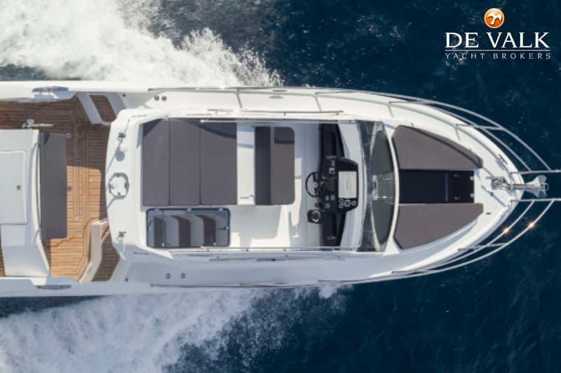 Een bovenaanzicht van een witte motorboot met grijze kussens en een houten dek, varend op blauw water. — Galeon 300 Fly