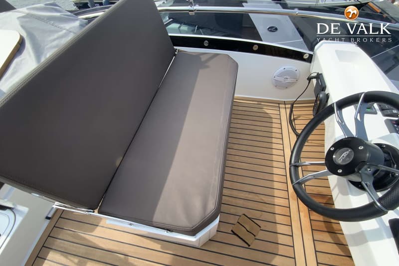 Een bootinterieur met een stuurwiel, een bank met grijze kussens en een houten dek.