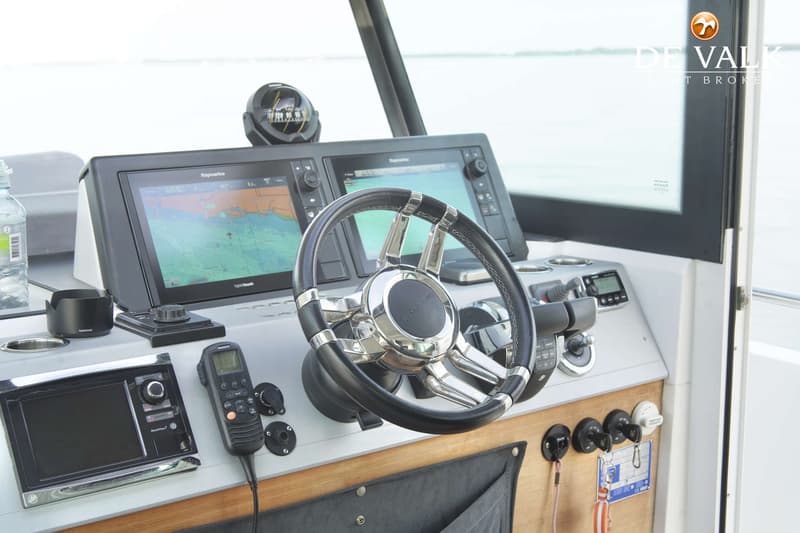Een stuurstand met een stuur, twee Raymarine schermen, een kompas, een marifoon en diverse bedieningselementen.