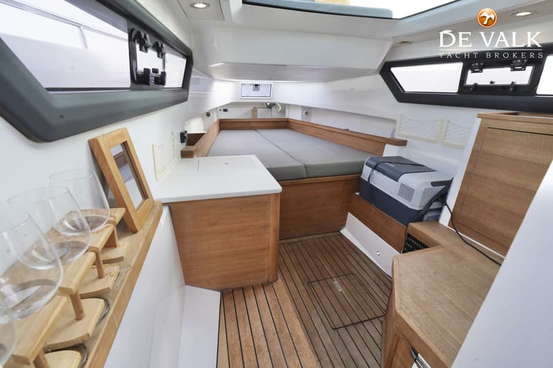 De foto toont een kajuit met een bed, houten vloer, ramen en een koelbox. — Axopar 37 AC