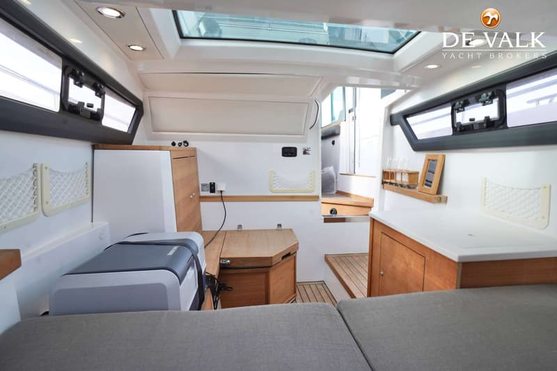De foto toont het interieur van een boot met een koelbox, houten kasten, een bank en een glazen dak. — Axopar 37 AC