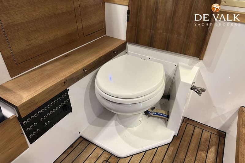 Een wit scheepstoilet met houten accenten en een bedieningspaneel is zichtbaar.
