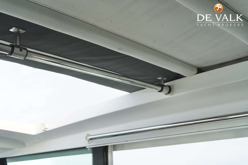 De foto toont een interieur van een boot met een wit plafond, een zwart zonnescherm en twee horizontale metalen stangen.
