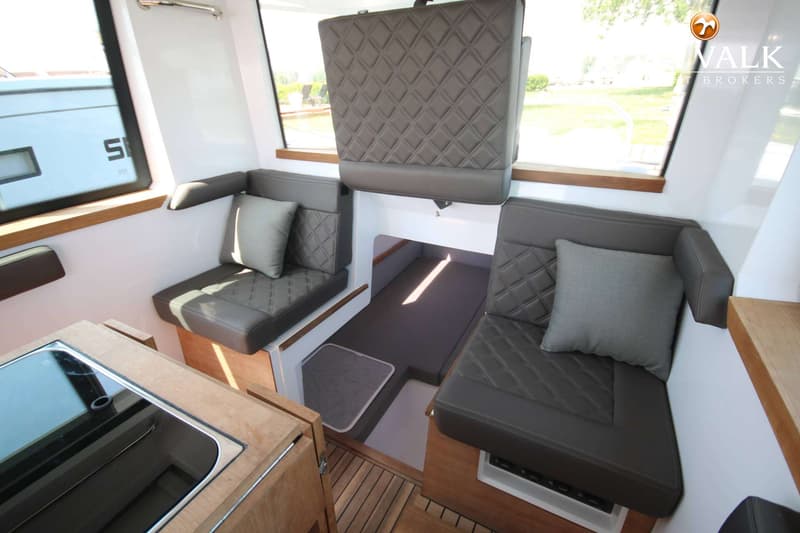 De foto toont het interieur van een boot met twee zitbanken, een bed, een kookplaat en een gootsteen. — Axopar 37 AC