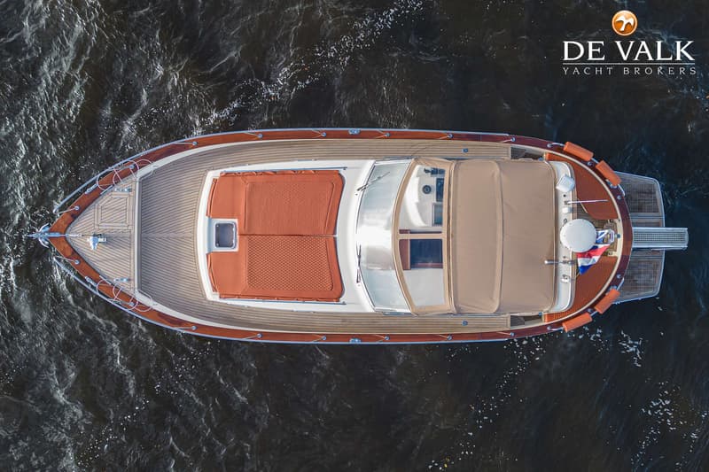 Een bovenaanzicht van een motorboot met een houten dek en oranje kussens, varend op donker water. — Apreamare 11