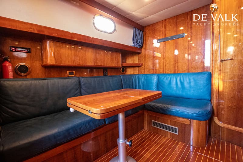 Een houten interieur van een boot met een U-vormige bank met donkerblauwe kussens en een houten tafel. — Apreamare 11