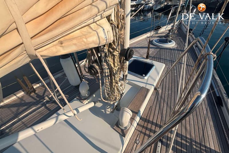 Een dek van een zeilboot met een opgerold zeil, touwen, een luik en een reling. — Hutting 40