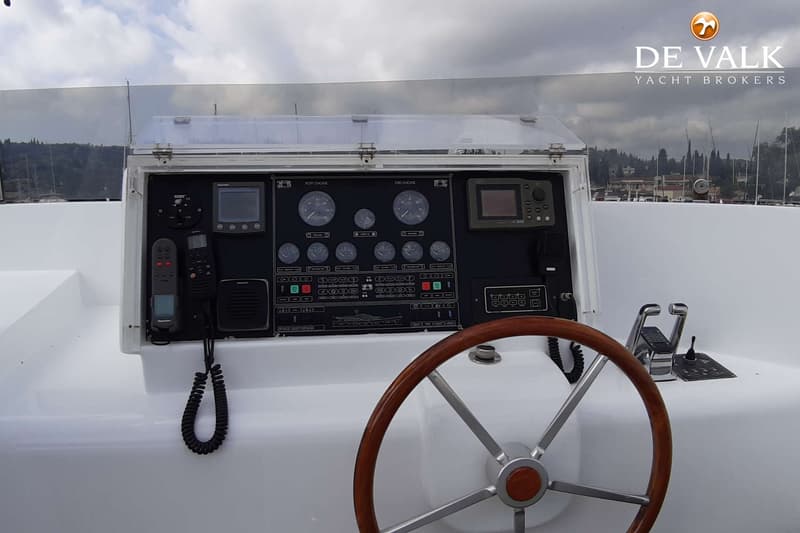 Een stuurwiel met houten rand en een dashboard met meters, schermen en bedieningselementen zijn zichtbaar.