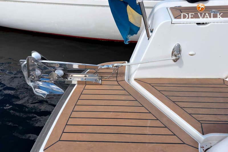 Een deel van een boot met een teakhouten dek, een roestvrijstalen anker en een blauw-gele vlag. — Nimbus W9