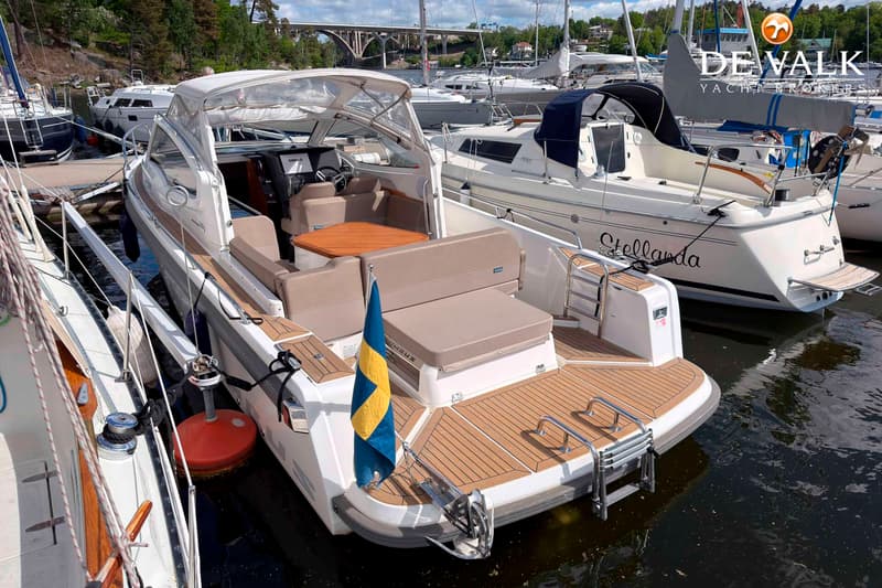 Een witte motorboot met een Zweedse vlag, houten dek en beige kussens ligt afgemeerd in een haven. — Nimbus W9