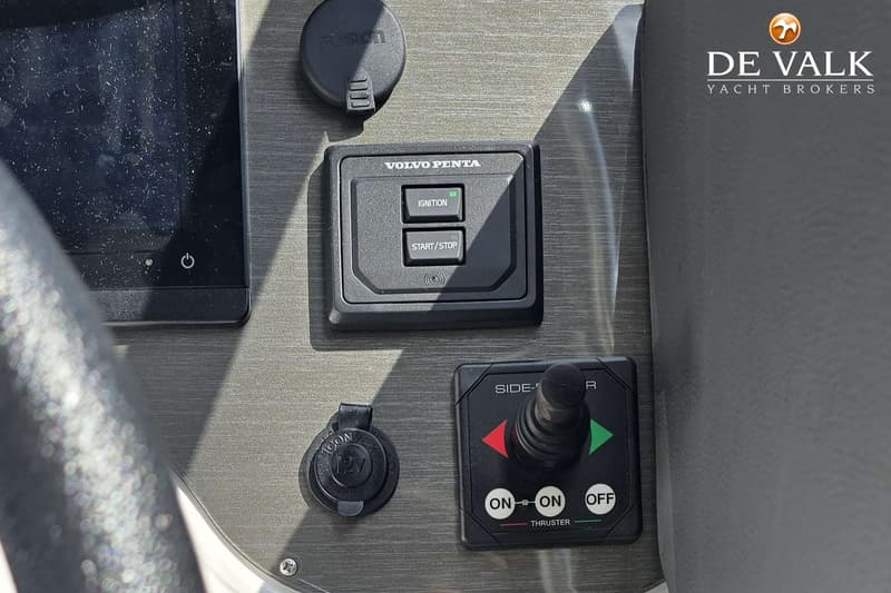 Een detail van een dashboard met een Volvo Penta start/stop-paneel, een thruster-bediening en een 12V-aansluiting.