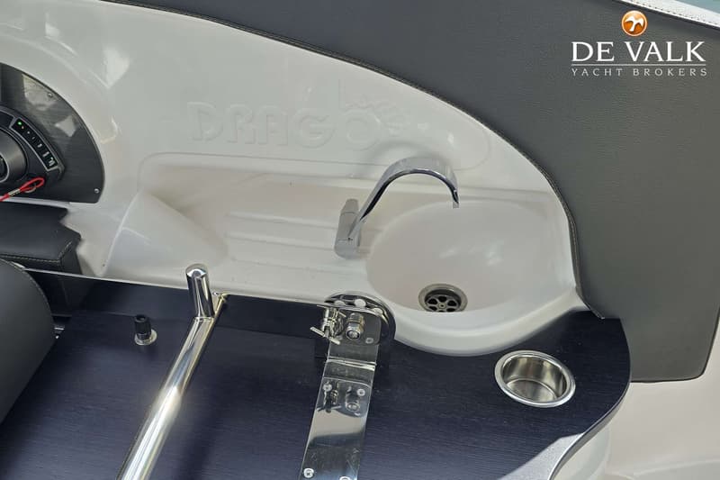 Een detailfoto van een bootinterieur met een wasbak, kraan, bekerhouder en het woord "DRAGOS" in reliëf.