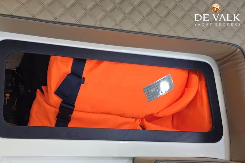 Een oranje reddingsvest met een donkerblauwe band en gesp ligt in een opbergvak.
