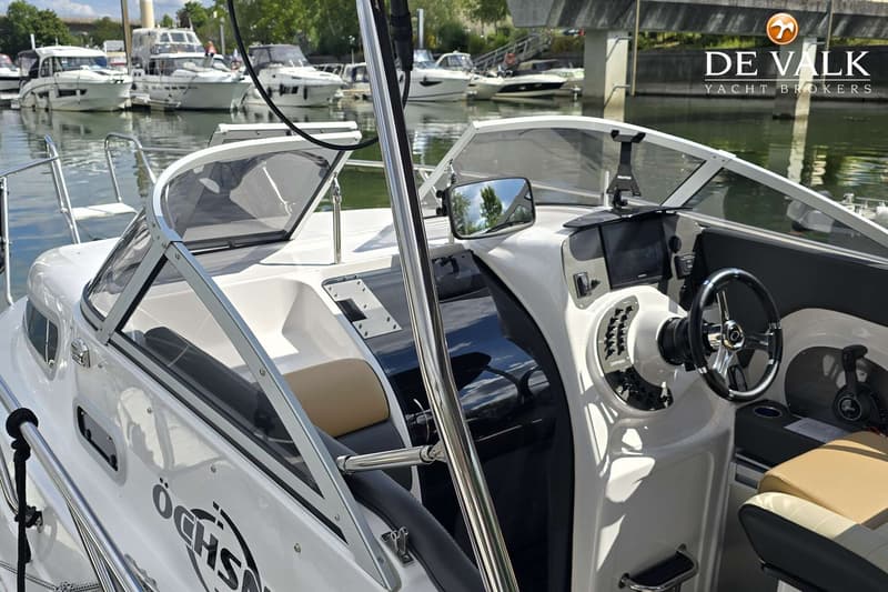 Een witte boot met een stuur, een spiegel en een Garmin-scherm, liggend in een haven met andere boten. — Öchsner SR 25