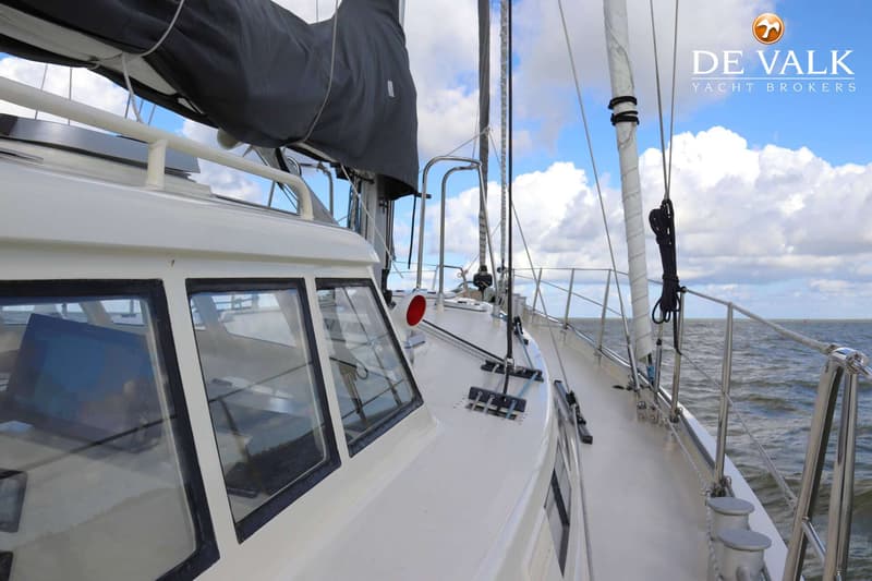 Een witte zeilboot met een donkergrijs zeil en een kajuit met ramen, varend op water onder een bewolkte hemel. — Aluyacht 49