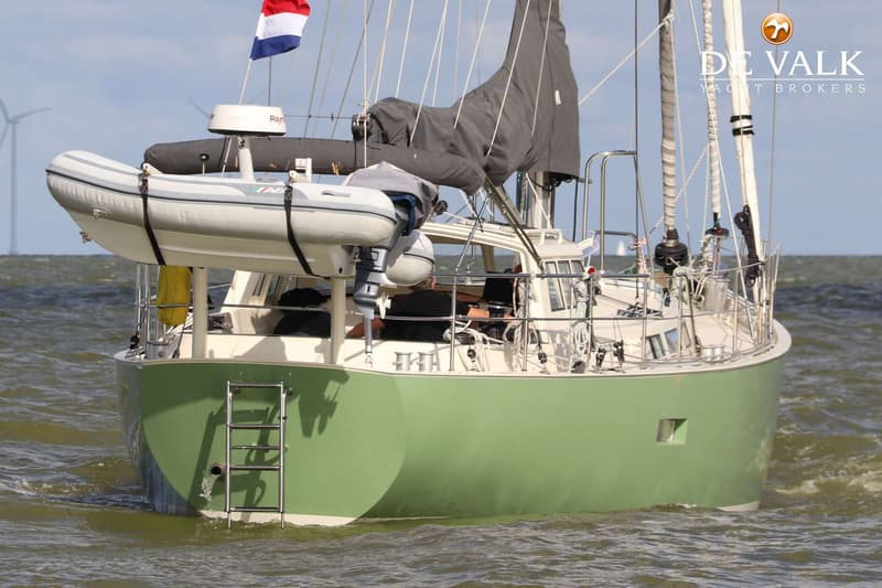Een groene zeilboot met een rubberboot en een Nederlandse vlag vaart op golvend water. — Aluyacht 49