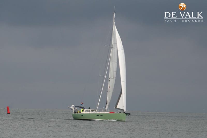 Een groene zeilboot met witte zeilen vaart op het water onder een grijze lucht, met een rode boei links. — Aluyacht 49