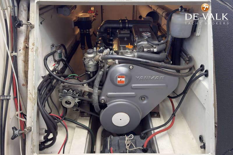 Een Yanmar motor is zichtbaar in een motorruimte, omringd door slangen, kabels en een filter.