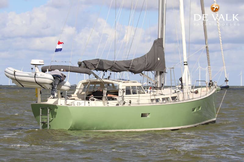 Een groene zeilboot met een bijboot en een Nederlandse vlag vaart op water met windmolens op de achtergrond. — Aluyacht 49
