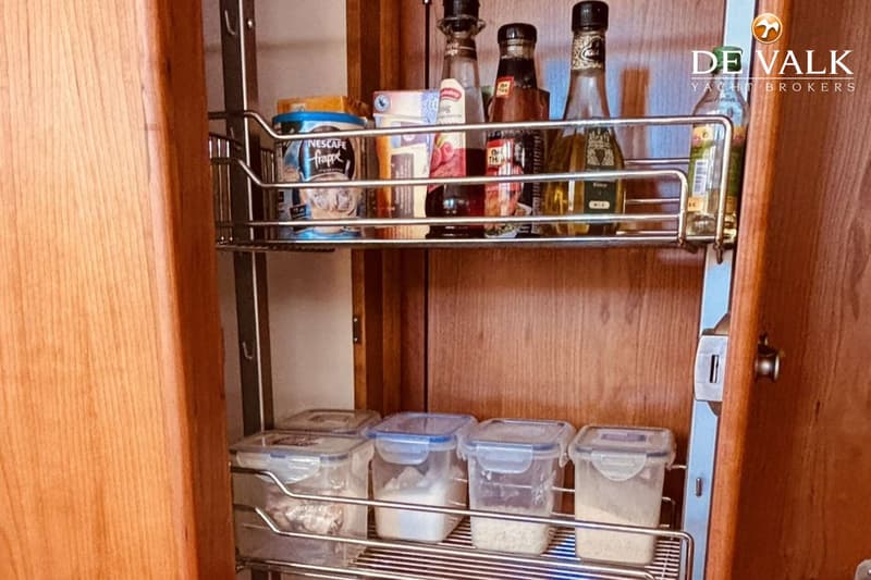 Een uittrekbaar rek met flessen, potten en doorzichtige bakjes met inhoud in een houten kast.