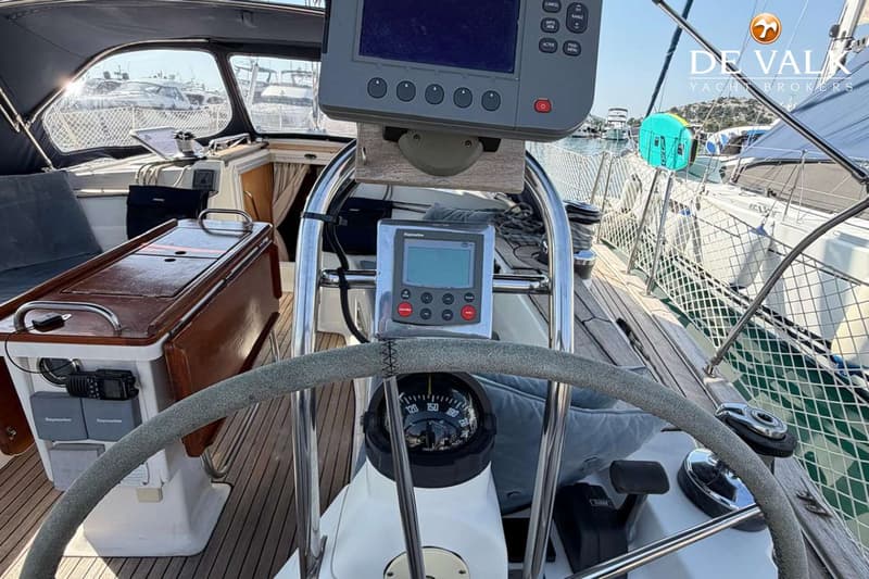 De foto toont een stuurstand met een kompas, twee Raymarine displays, een stuurwiel en een houten dek.