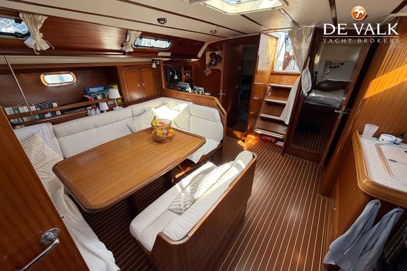 Een interieur van een boot met houten wanden en vloer, een witte bank met kussens, een houten tafel en een kombuis.