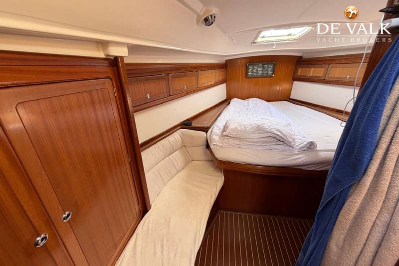 De foto toont een kajuit met een bed, een bankje, houten kasten en een houten vloer met lichte strepen. — Bavaria 47 Cruiser