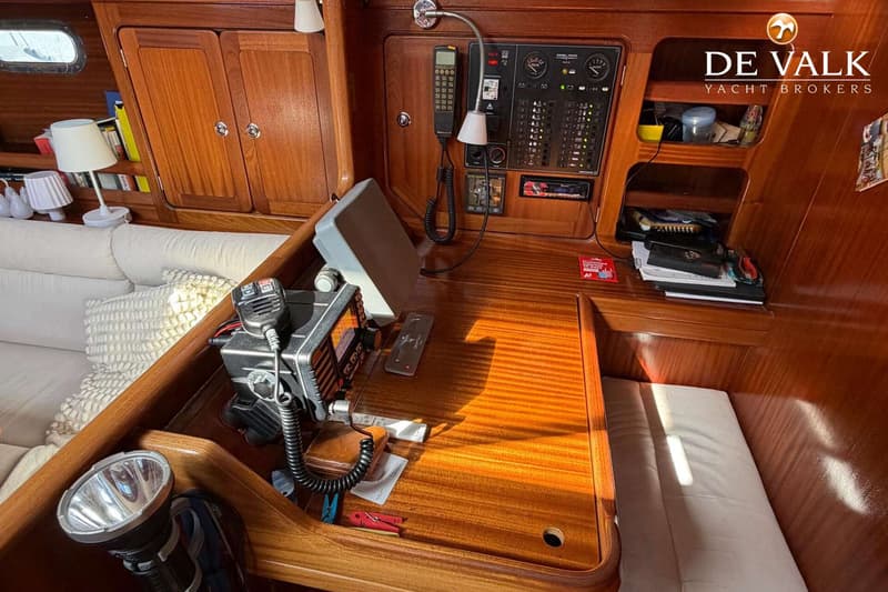 Een houten interieur met een navigatiehoek, communicatieapparatuur, een schakelpaneel en een bank met kussens.