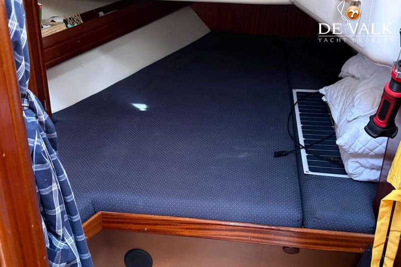 Een kajuit met een donkerblauw gestippeld matras, een wit kussen, een opvouwbaar zonnepaneel en een zaklamp.