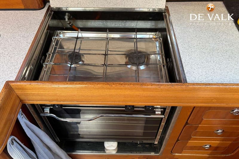 Een ingebouwd fornuis met twee pitten en een oven eronder, omringd door houten kasten en een aanrechtblad.