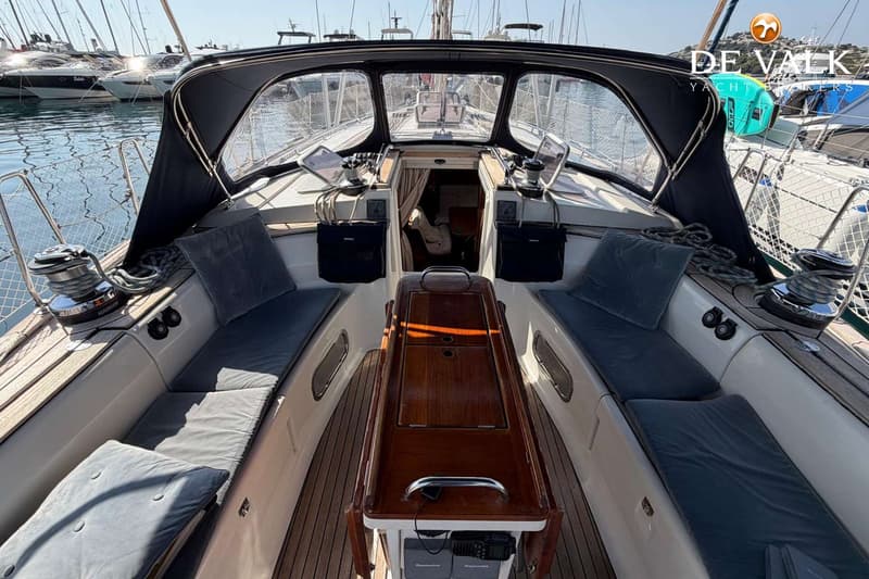 Een bovenaanzicht van de kuip van een zeilboot met een donkerblauwe buiskap, teakhouten dek en grijze kussens.