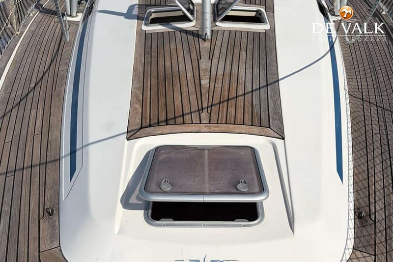 Een bovenaanzicht van het dek van een boot met houten planken en witte opbouw, inclusief luiken. — Bavaria 47 Cruiser