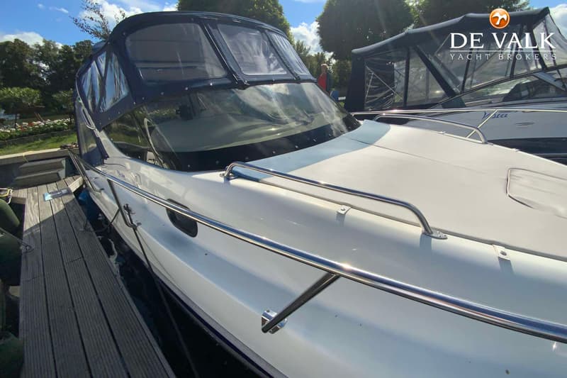 Een witte boot met een blauwe kap en een voorruit ligt aangemeerd aan een houten steiger. — Saver 750 Cabin