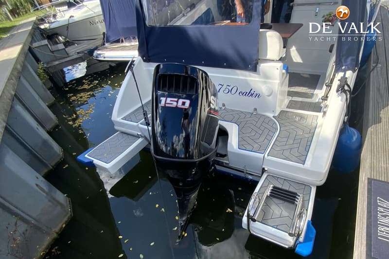 Een witte boot met een zwarte buitenboordmotor van 150 pk, liggend in het water naast een kade. — Saver 750 Cabin