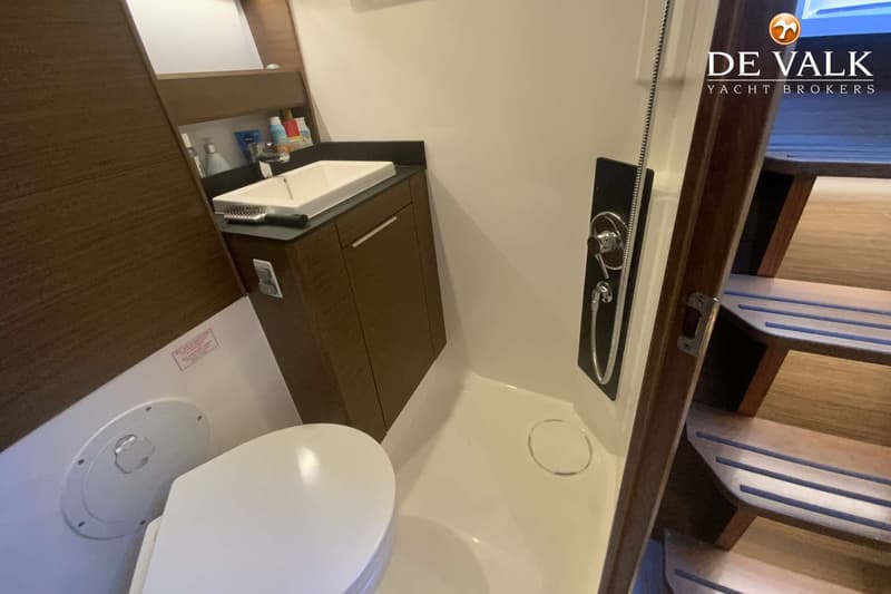 Een badkamer met een toilet, een wastafel met spiegel en een douchecabine, met een trap aan de rechterkant.