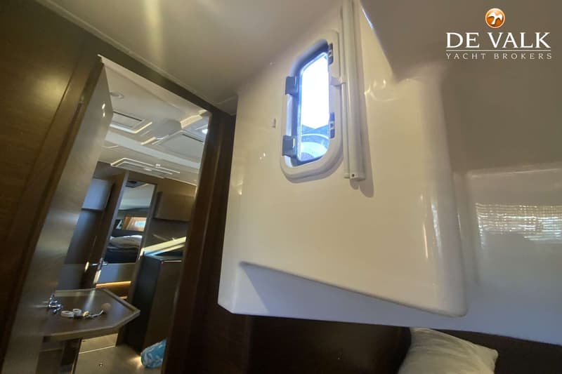 Een interieur van een boot met een patrijspoort, een doorgang naar een andere ruimte en een deel van een bed met een kussen.