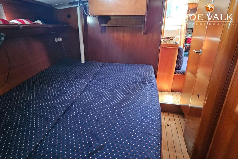 Een kajuit met een donkerblauw gestippeld matras, houten wanden en een houten vloer. — Beneteau 50