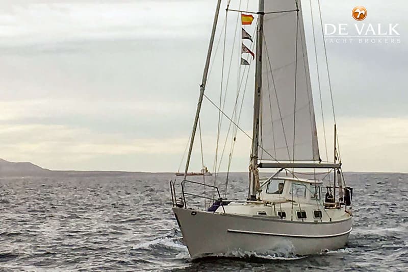 Een zeilboot met een wit zeil vaart op zee, met land in de verte onder een bewolkte lucht. — Overseas 35