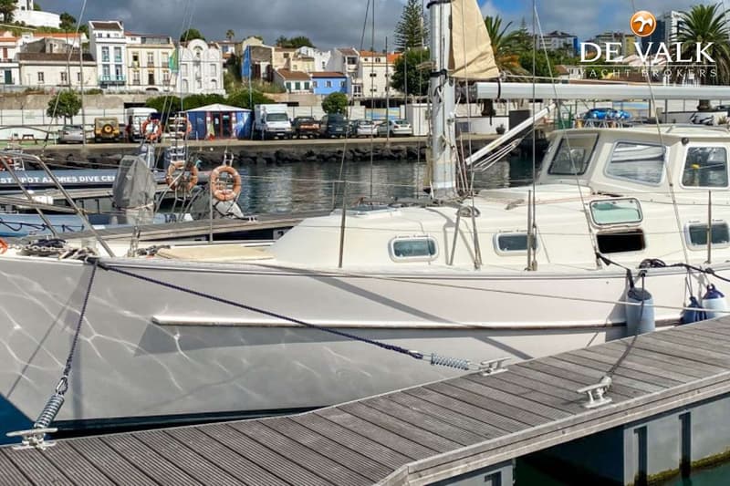 Een witte zeilboot ligt aangemeerd aan een houten steiger, met een stad op de achtergrond. — Overseas 35