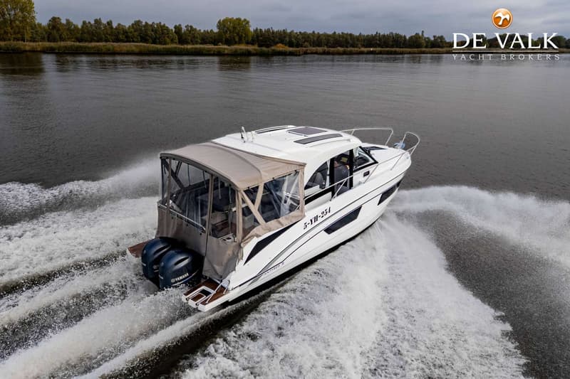 Een witte motorboot met twee buitenboordmotoren vaart over water, met een bosrijke oever op de achtergrond.
