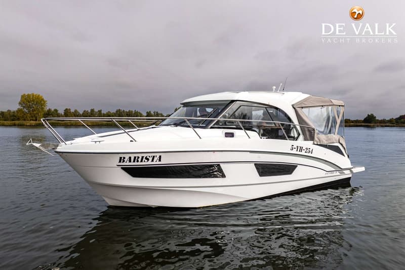 Een witte motorboot met de naam "BARISTA" en registratienummer "5-YH-254" drijft op water onder een bewolkte lucht.