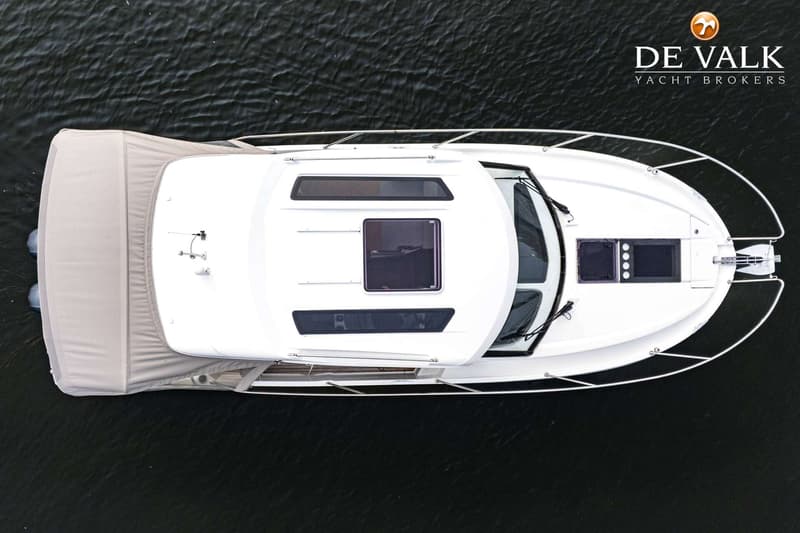 Een witte motorboot met een beige afdekzeil aan de achterzijde, gezien van bovenaf op donker water.