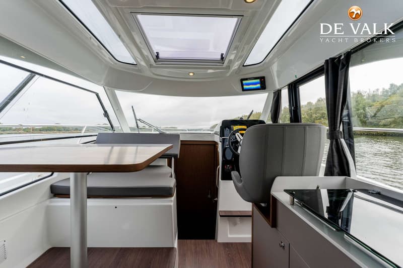 De foto toont het interieur van een boot met een stuurstand, zitplaatsen, een tafel en een kookplaat.