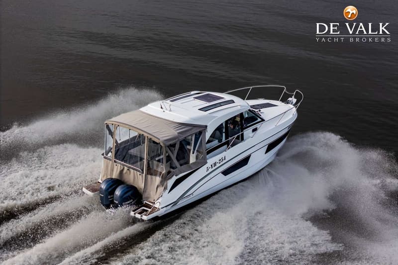 Een witte motorboot met twee buitenboordmotoren vaart over donker water en laat een schuimspoor achter.