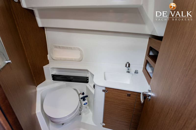 Een witte badkamer met een toilet, wastafel, kraan en houten kastjes.