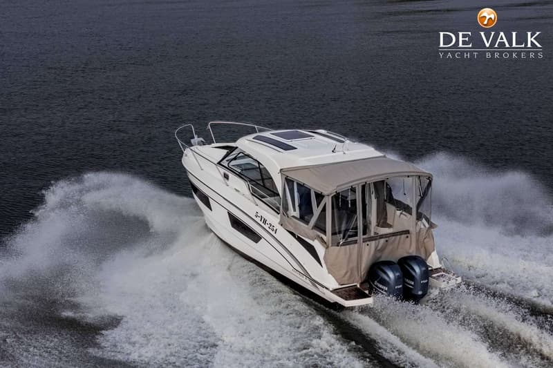 Een witte motorboot met twee buitenboordmotoren vaart over donker water en laat een kielzog achter.